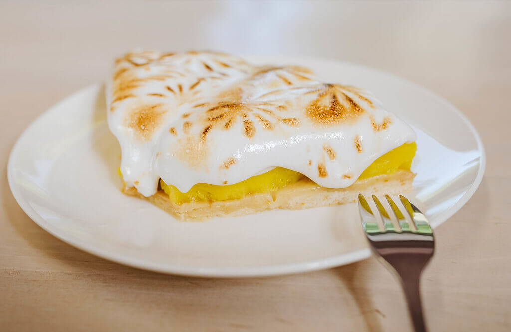 Marco Verch - Ein Stück Zitronencreme Tarte auf einem weißen Teller, neben einer Gabel